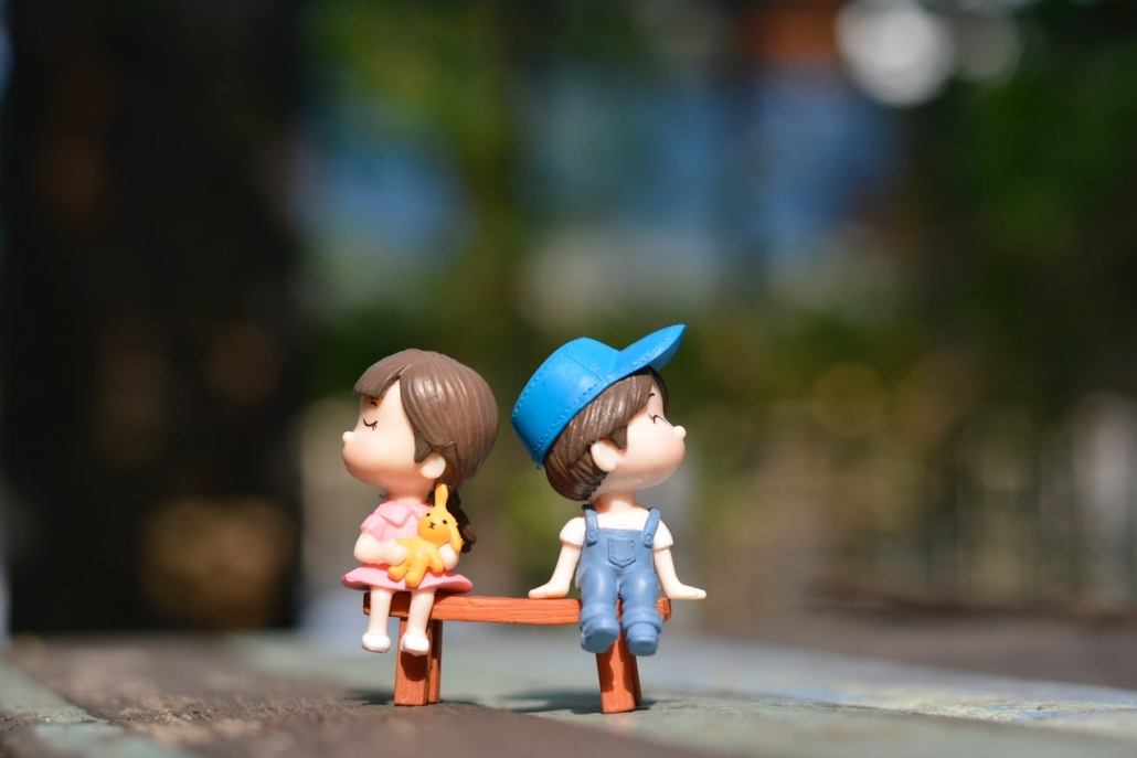 Spielzeugfiguren: Bub und Mädchen auf einer Bank. Beide typisch als Bub und Mädchen angezogen.